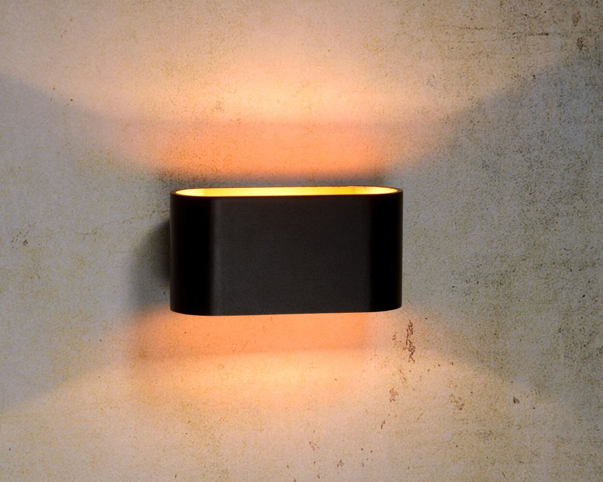 Applique murale noire allumée sur un mur texturé, halo lumineux vers le haut et le bas.
