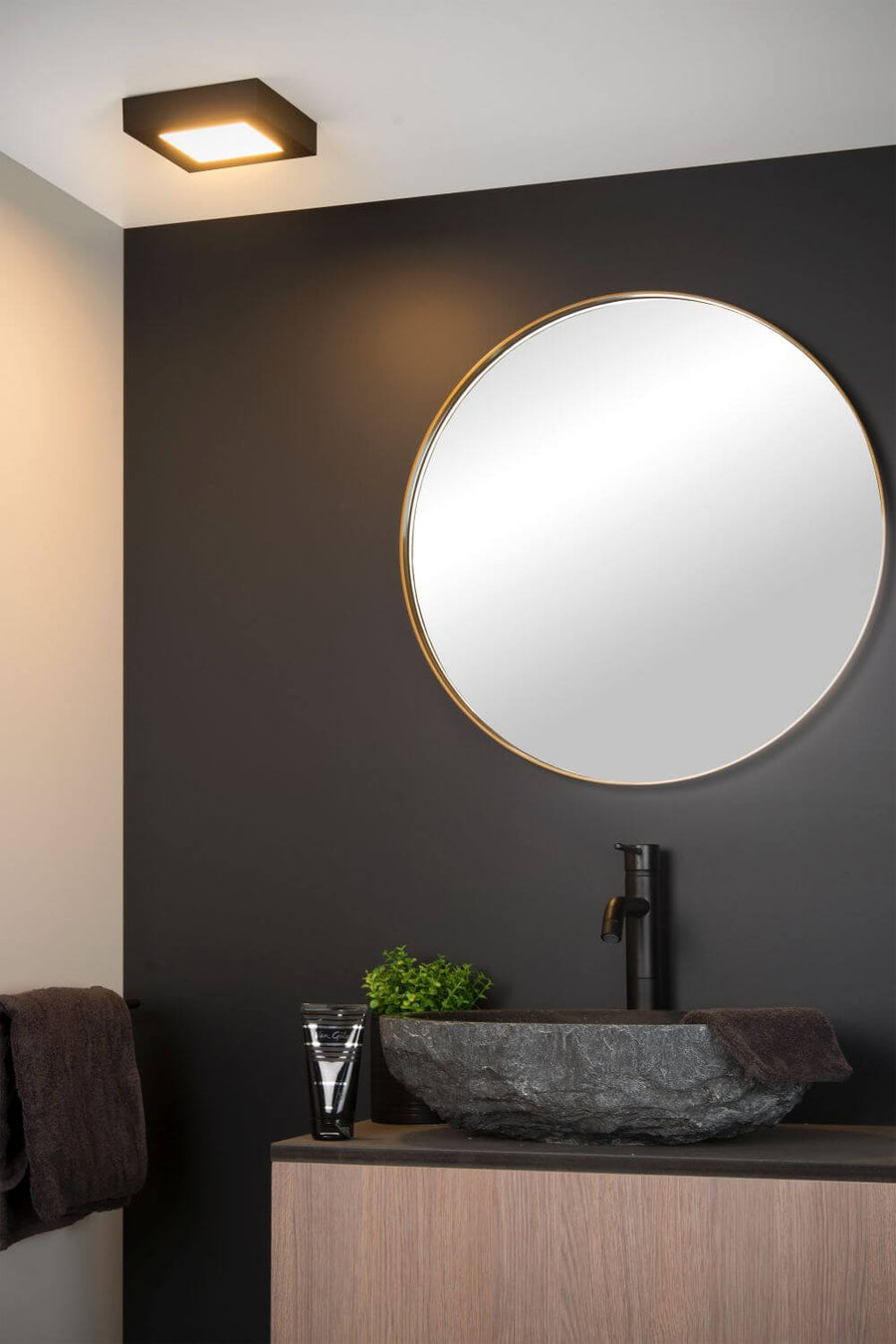 Vue rapprochée du plafonnier carré noir allumé, fixé au plafond au-dessus du miroir.