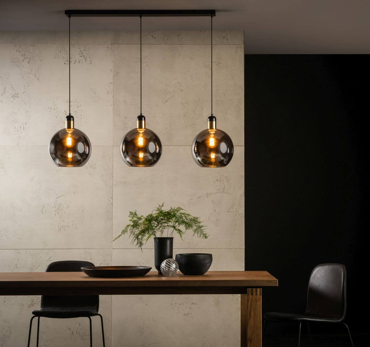 Vue en situation : trois globes lumineux suspendus au-dessus d'une table en bois et d'une plante verte.