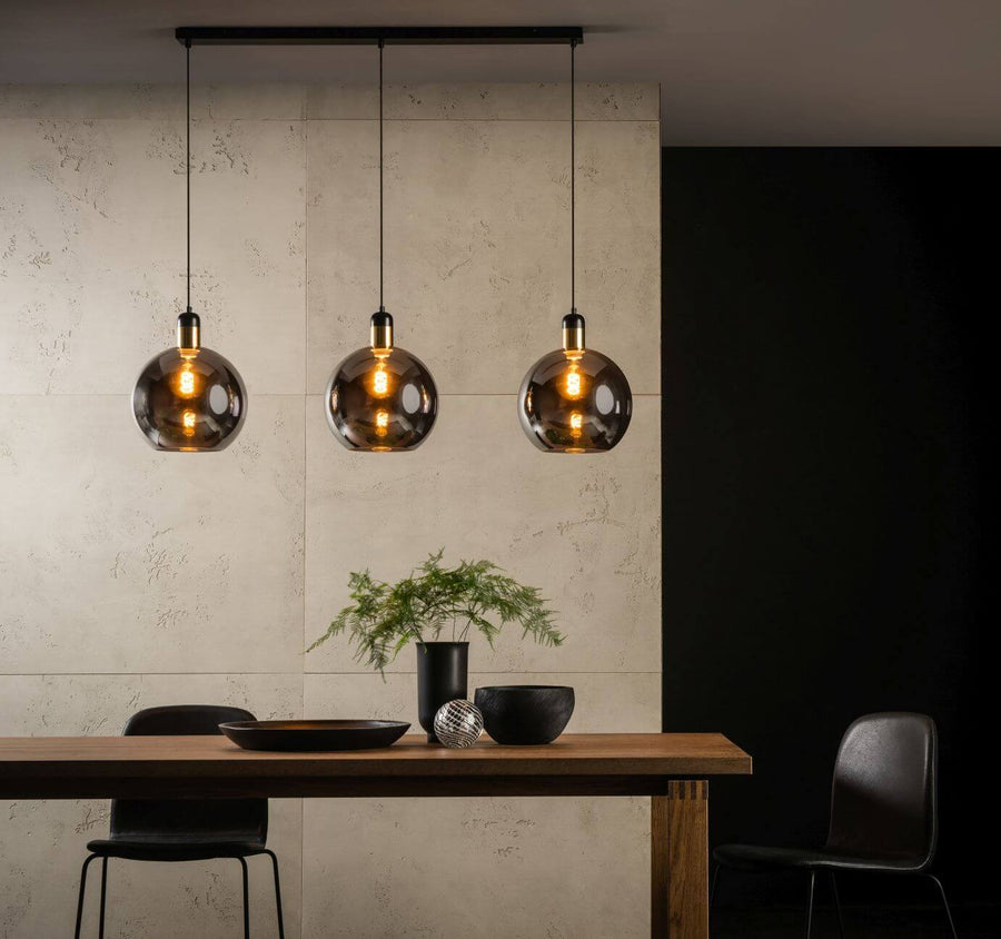 Vue en situation : trois globes lumineux suspendus au-dessus d'une table en bois et d'une plante verte.