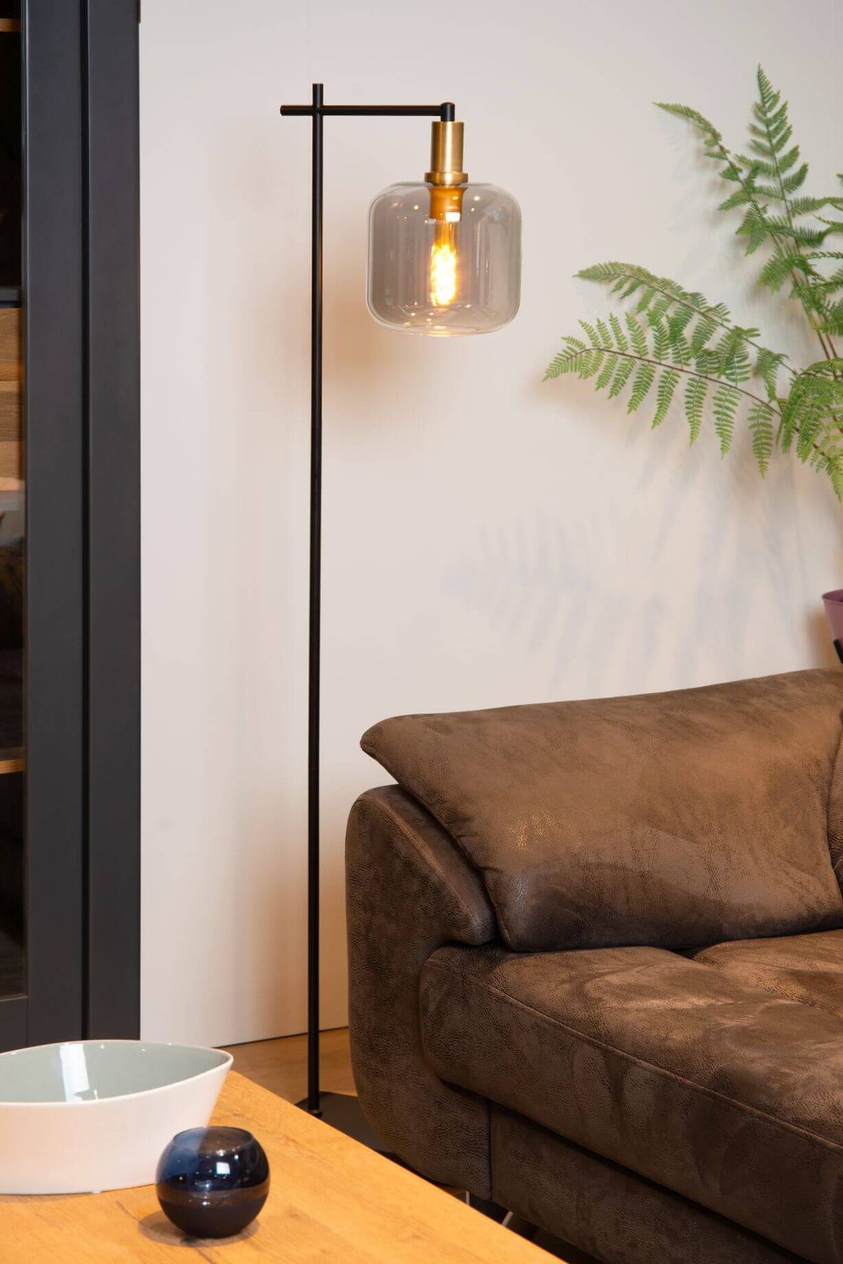 Détail du luminaire dans un intérieur, verre fumé et tige noire, reflets sur le mur.