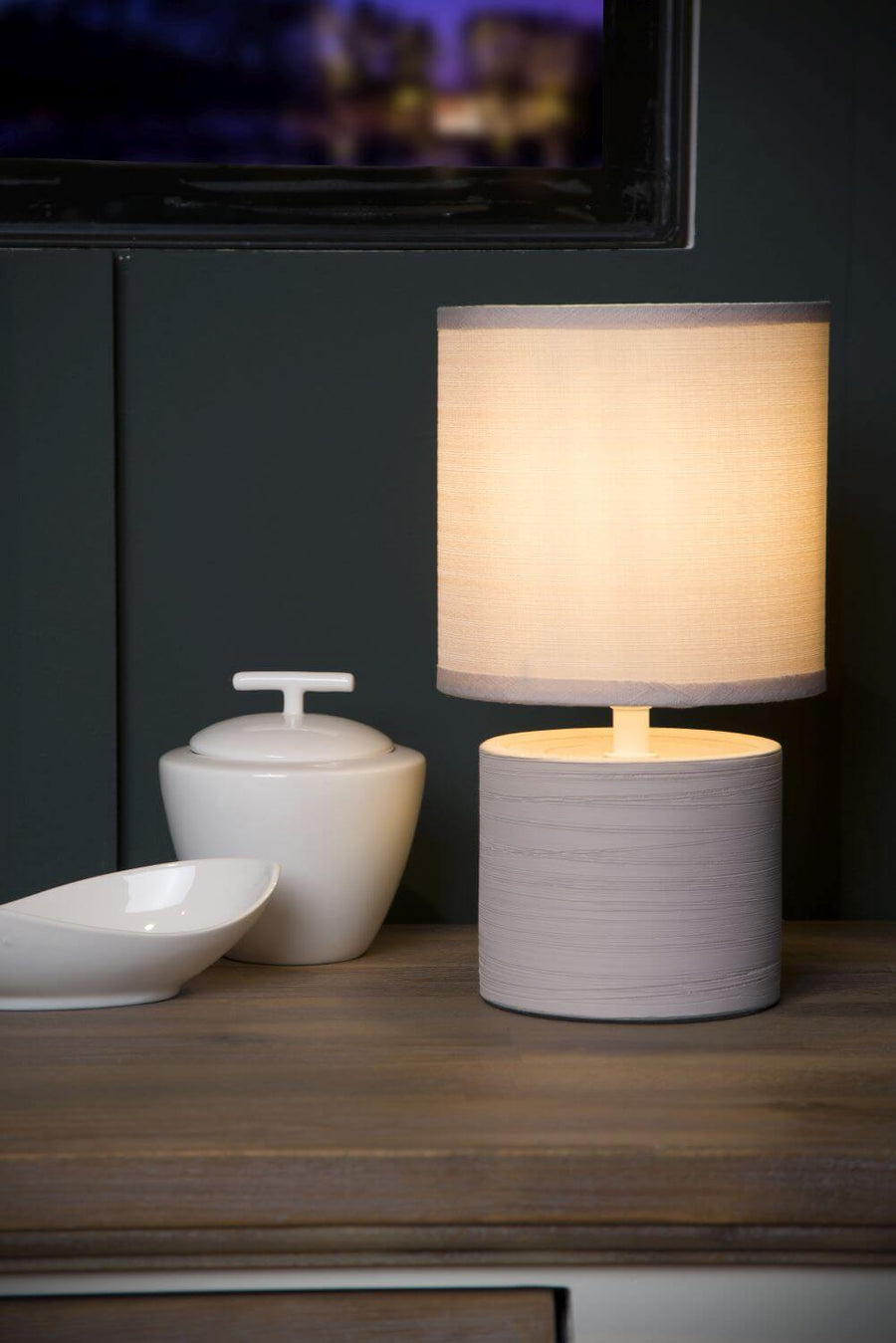 Vue rapprochée de la lampe allumée posée sur meuble, bols blancs décoratifs à côté.