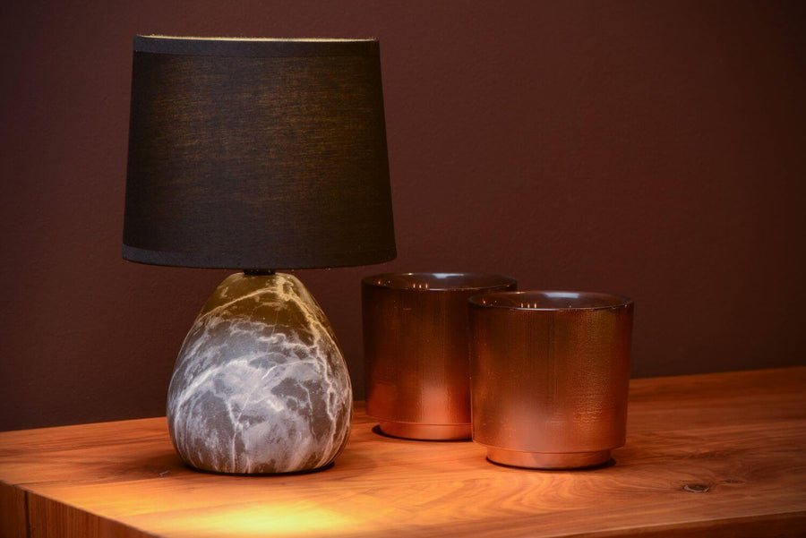 Gros plan de la lampe à poser, abat-jour noir et base marbrée sur fond sombre.