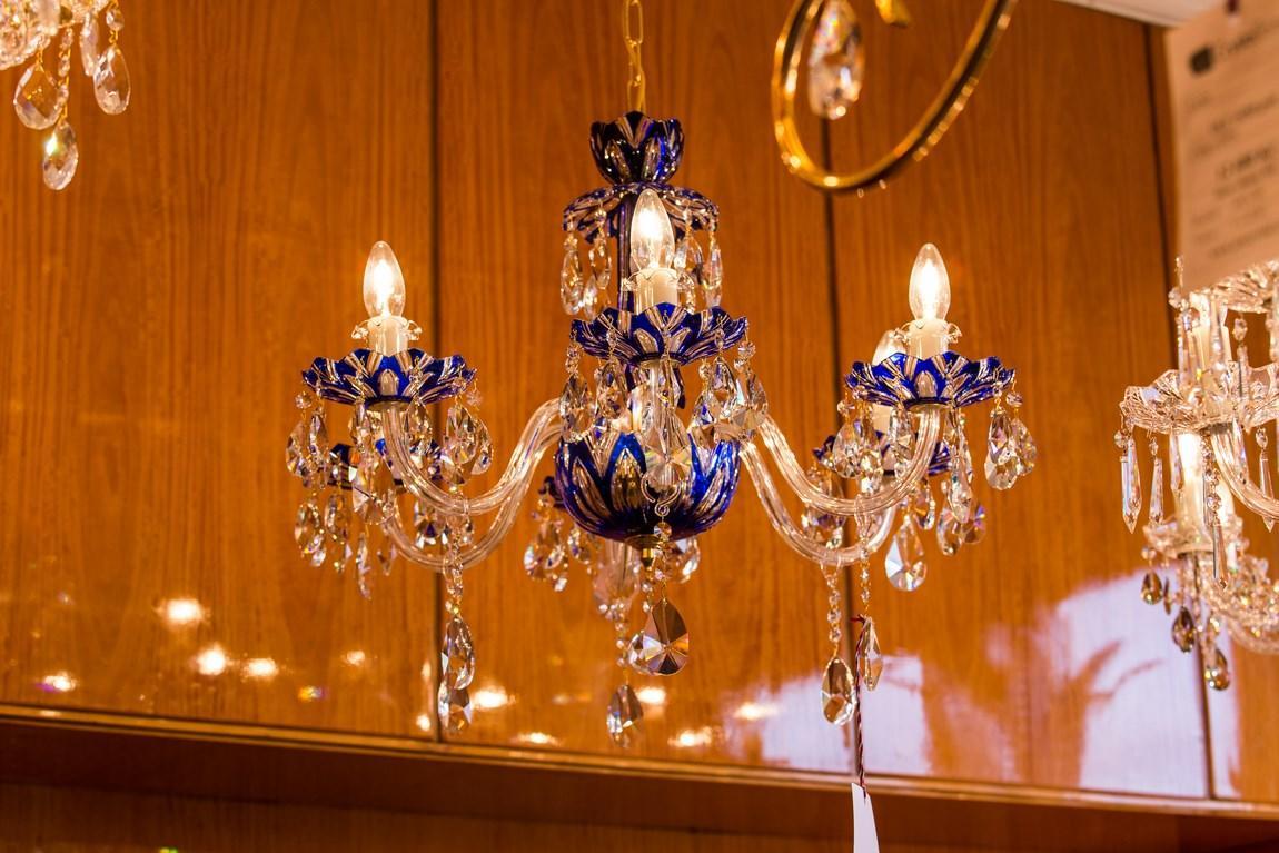 Lustre allumé suspendu devant un mur boisé, reflets dorés sur les pampilles