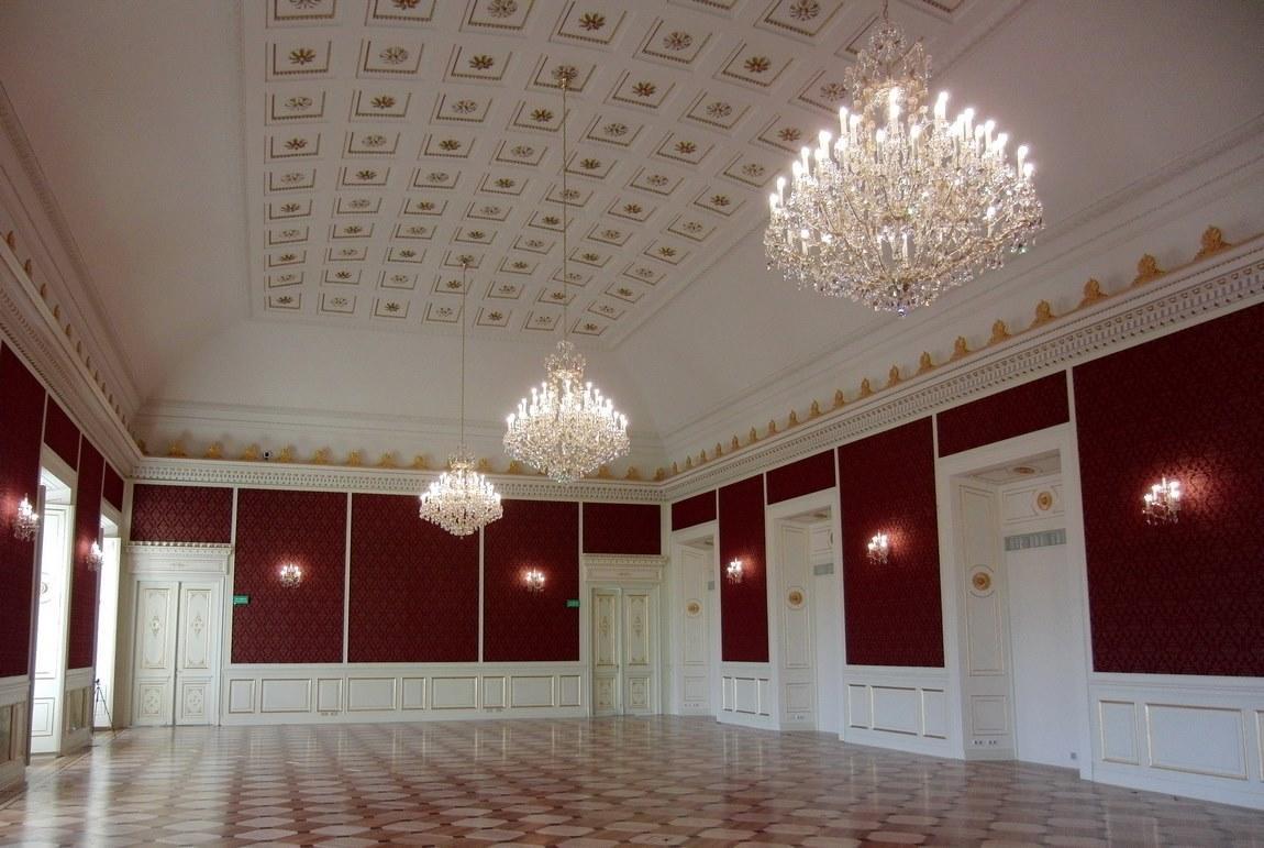 Salle de bal aux murs rouges, plusieurs lustres suspendus au plafond blanc