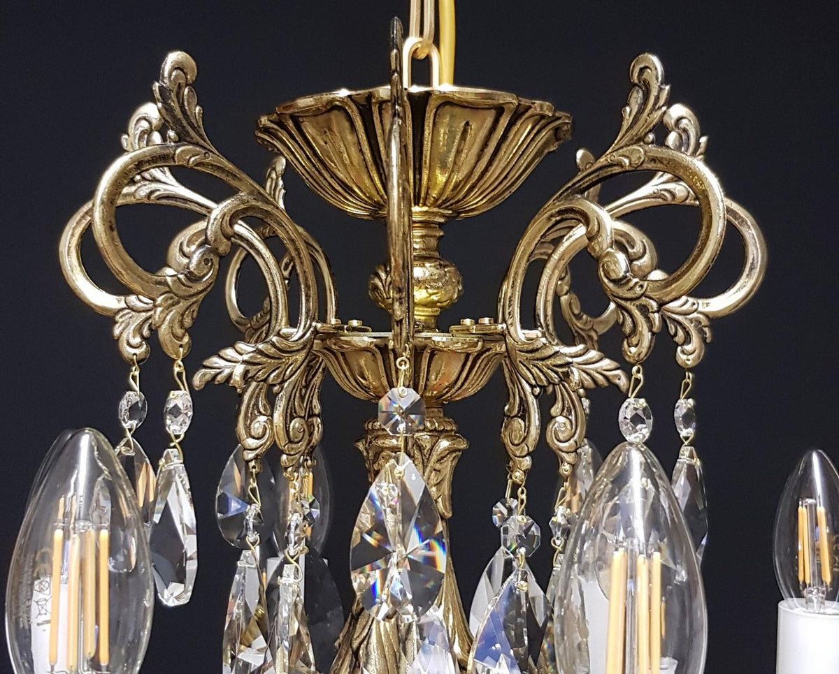 Gros plan du décor ciselé des bras recourbés et des gouttes de cristal facettées.