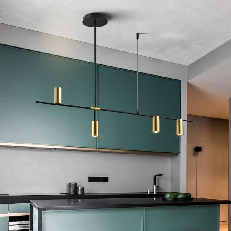 Luminaire suspendu à barre noire et cylindres laiton devant des meubles verts