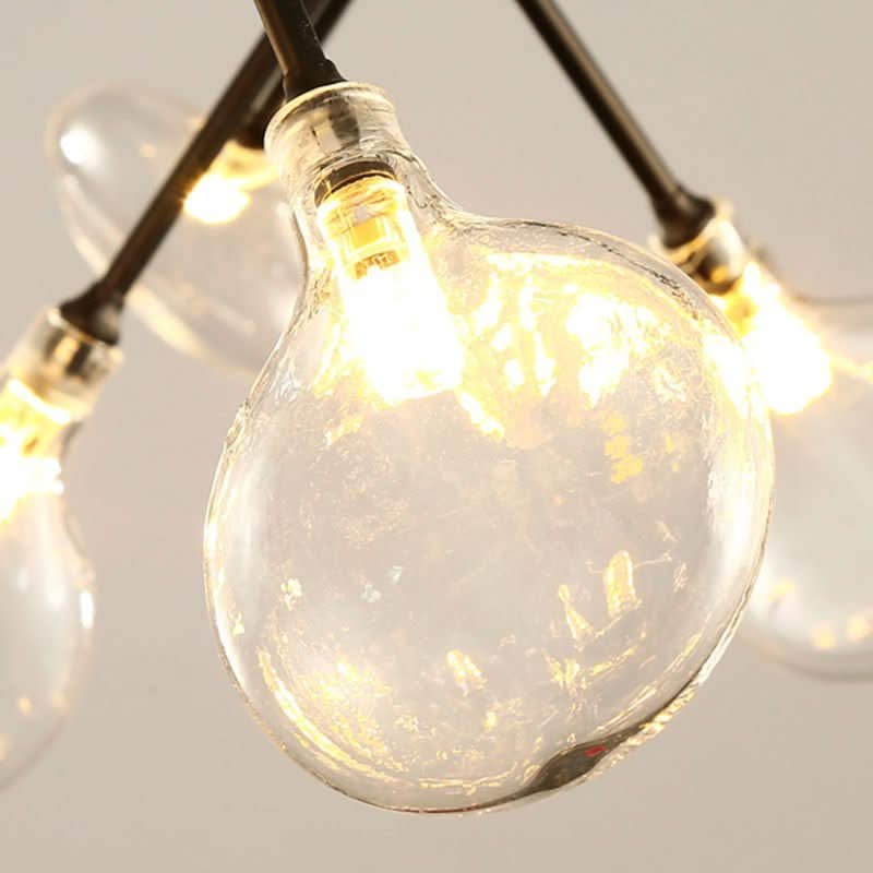 Gros plan sur une ampoule goutte en verre transparent, filament LED allumé.