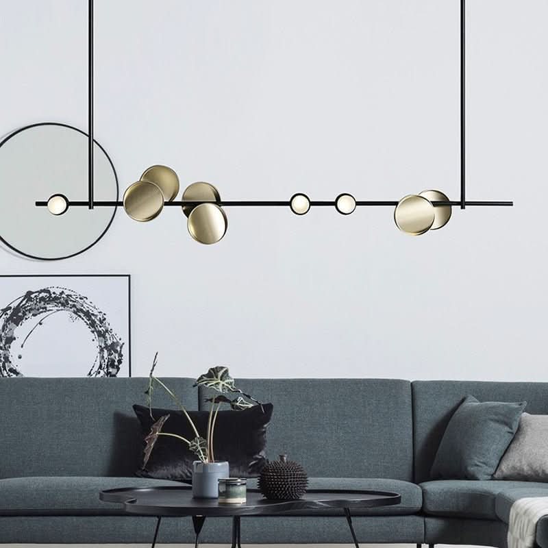 Suspension linéaire dorée installée dans un salon au-dessus d’un canapé gris.