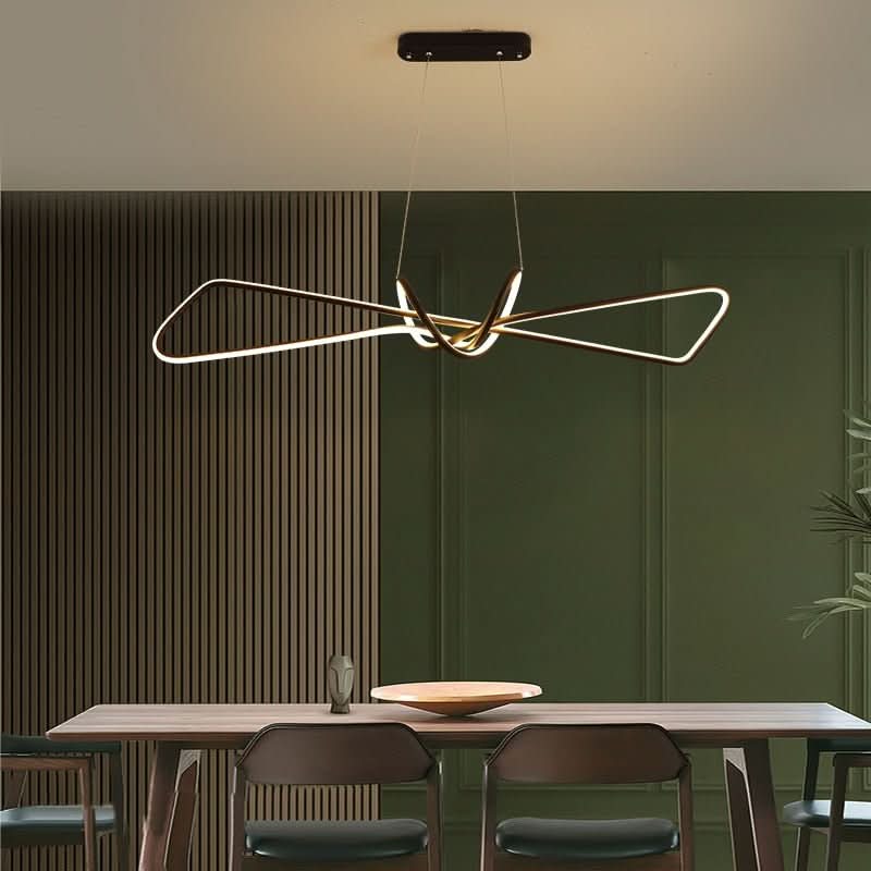Luminaire allumé devant un mur vert, table en bois et chaises sombres pour ambiance repas