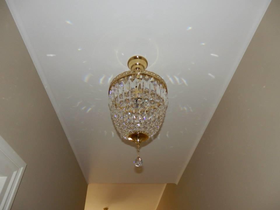 Luminaire allumé vu de dessous sur plafond blanc, reflets cristallins dispersés
