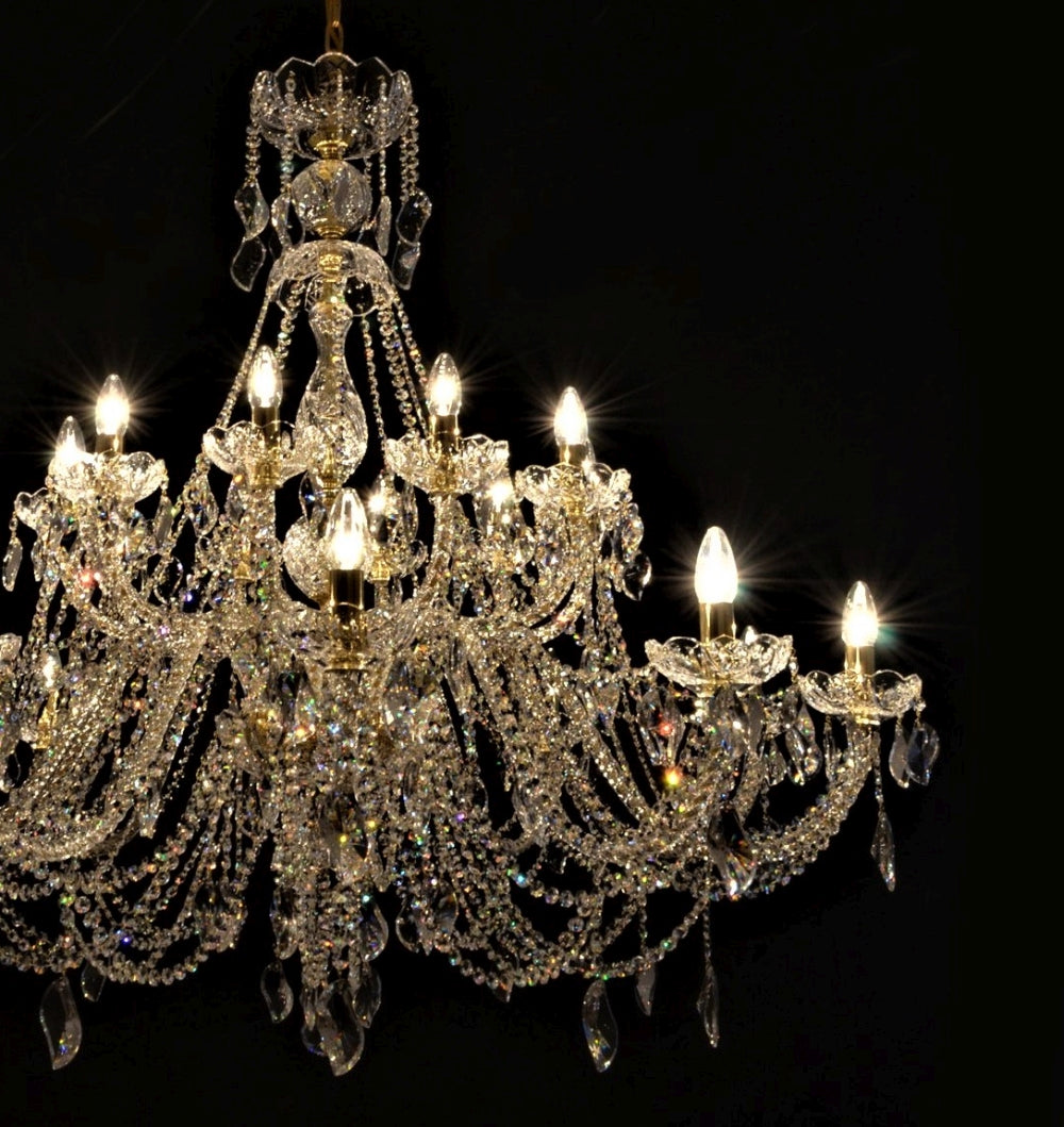 Gros plan du lustre en cristal allumé, montrant la structure dorée et les pendentifs.