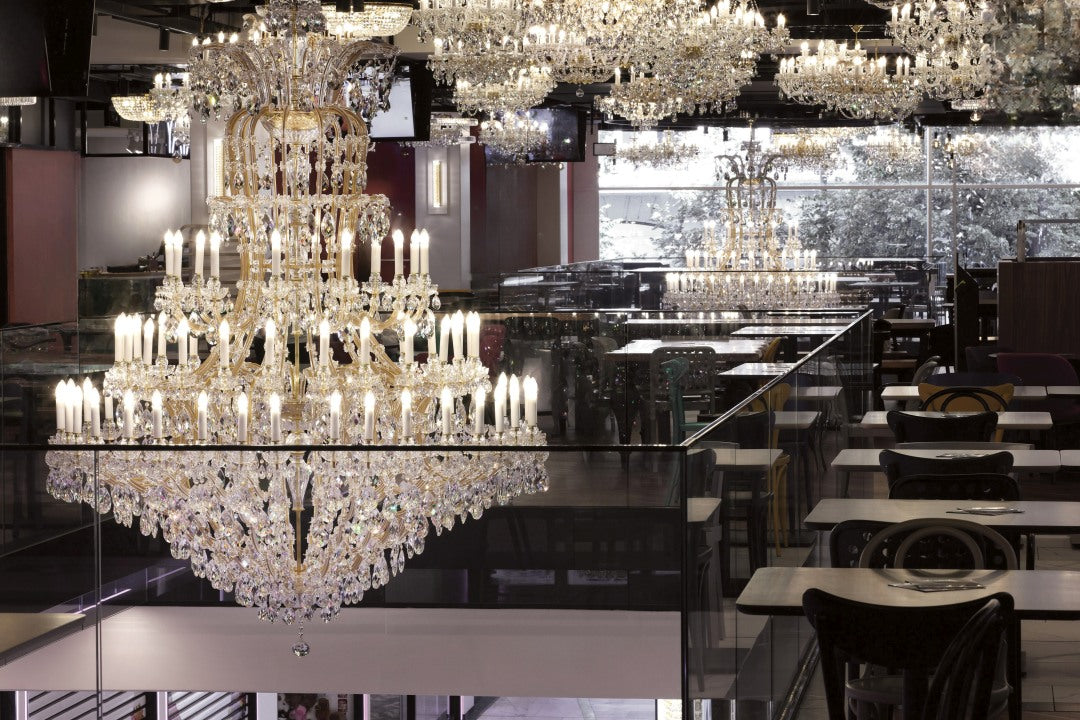 Lustre reflété dans un miroir de salle de restaurant, tables et chaises alignées.