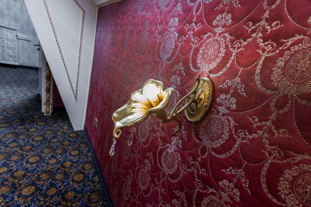Vue de l'applique dorée allumée sur un papier peint rouge dans un couloir.