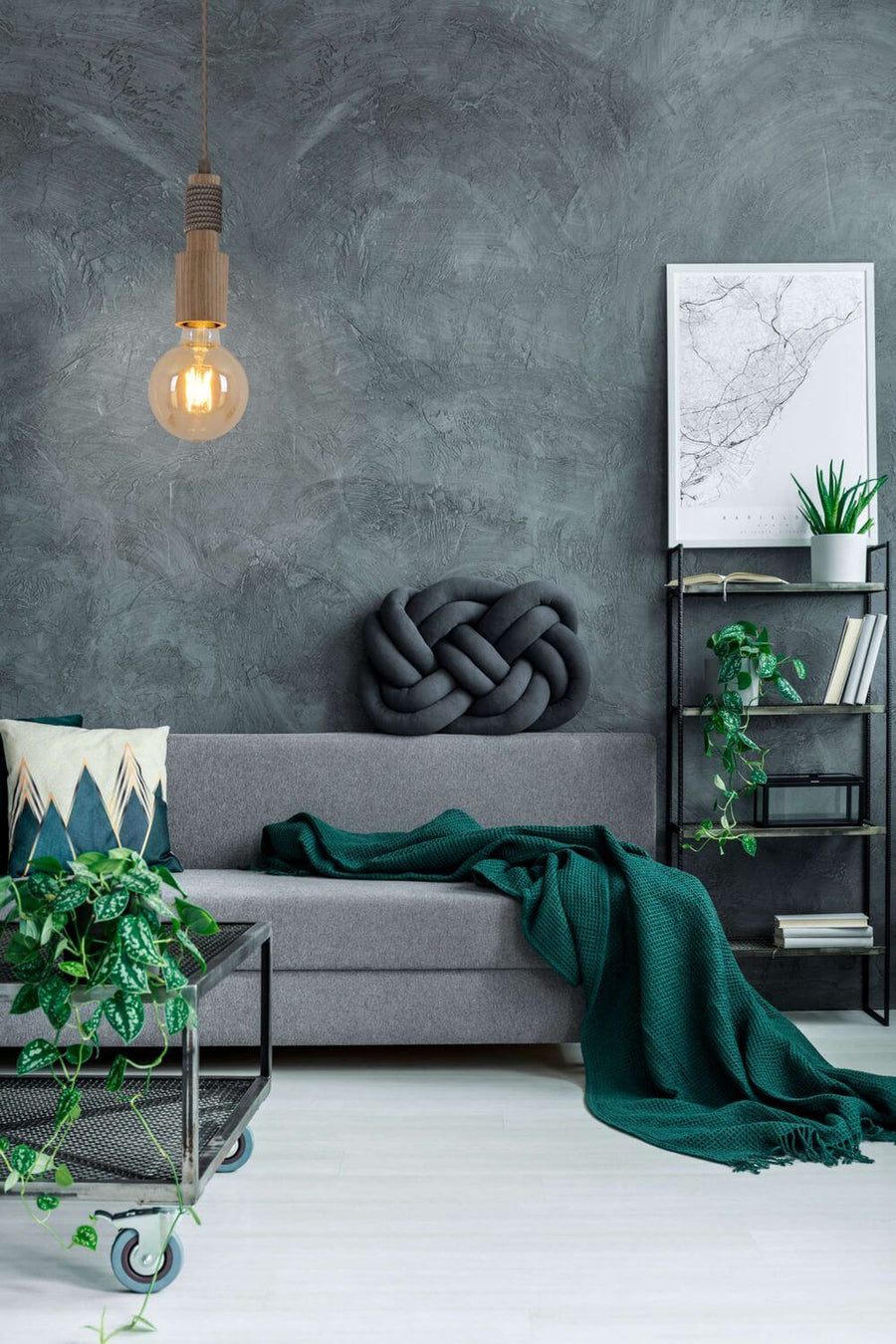 Suspension allumée dans un salon gris au mur béton, canapé et plaid vert