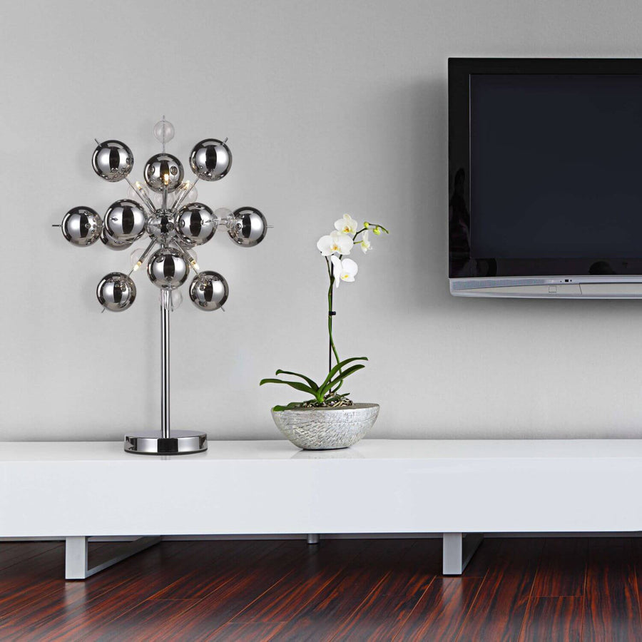 Lampe chromée posée sur meuble TV blanc, près d'une orchidée en pot.