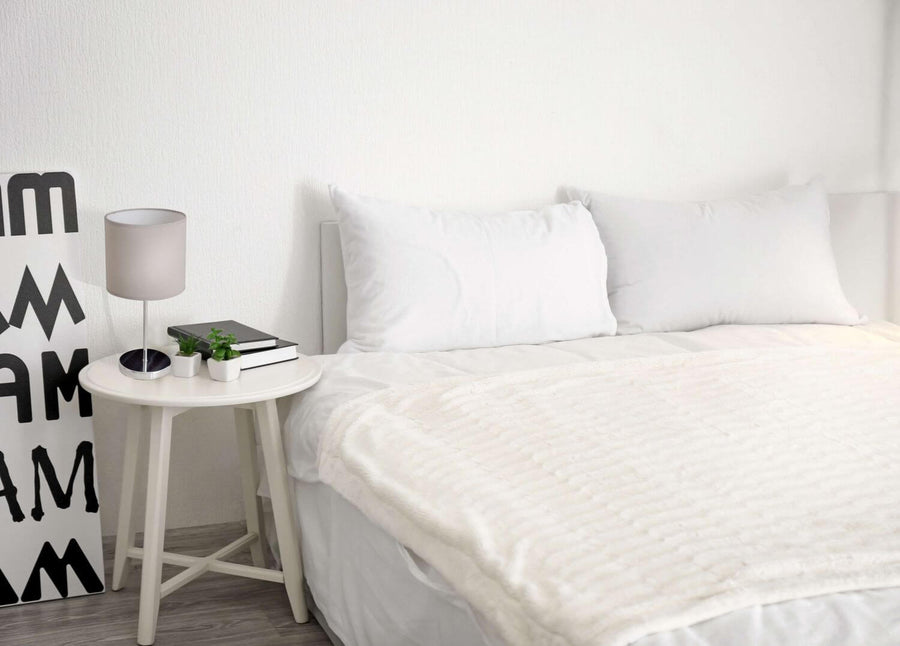Lampe grise posée sur une table de chevet blanche, près d'un lit dans une chambre claire.