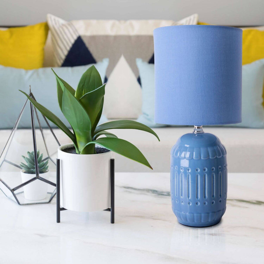 Lampe bleue sur table marbre, plante verte en pot et objets déco, canapé en arrière-plan.