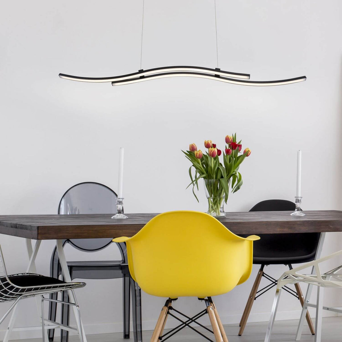 Suspension noire allumée au-dessus d'une table en bois avec chaises colorées
