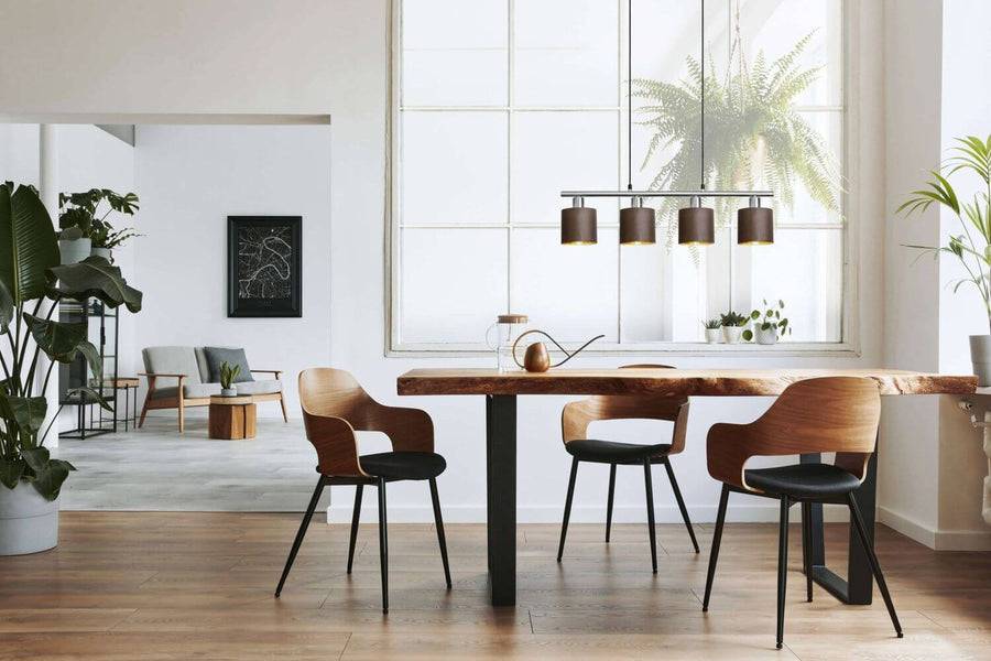 Vue large du séjour, suspension linéaire au-dessus de la table, fauteuils bois et plantes vertes