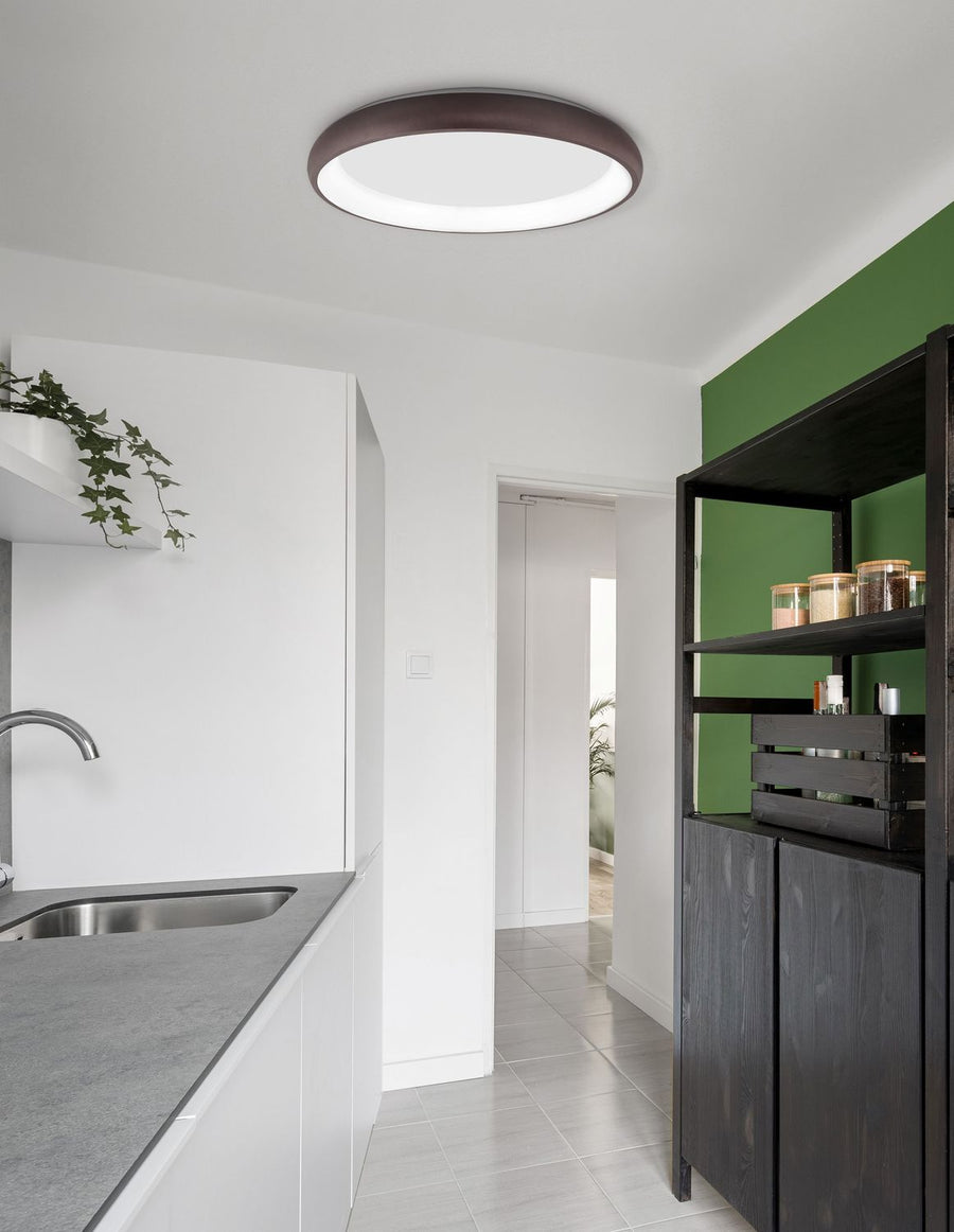 Plafonnier rond marron allumé au plafond d'une cuisine blanche et verte