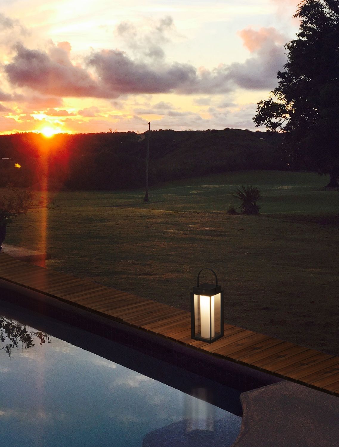 Luminaire extérieur allumé au bord d'une piscine au coucher du soleil