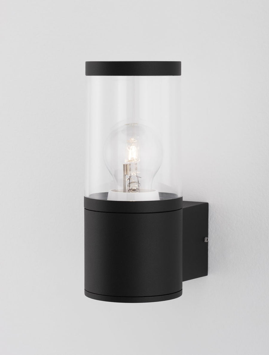 Gros plan sur le bas du luminaire et sa platine noire fixée au mur.