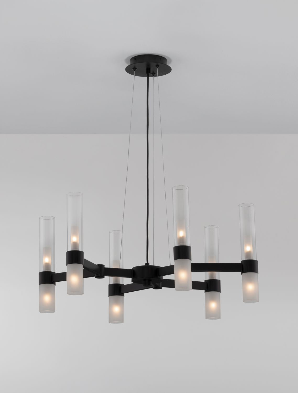 Luminaire suspendu allumé avec ampoules visibles à travers les cylindres en verre.