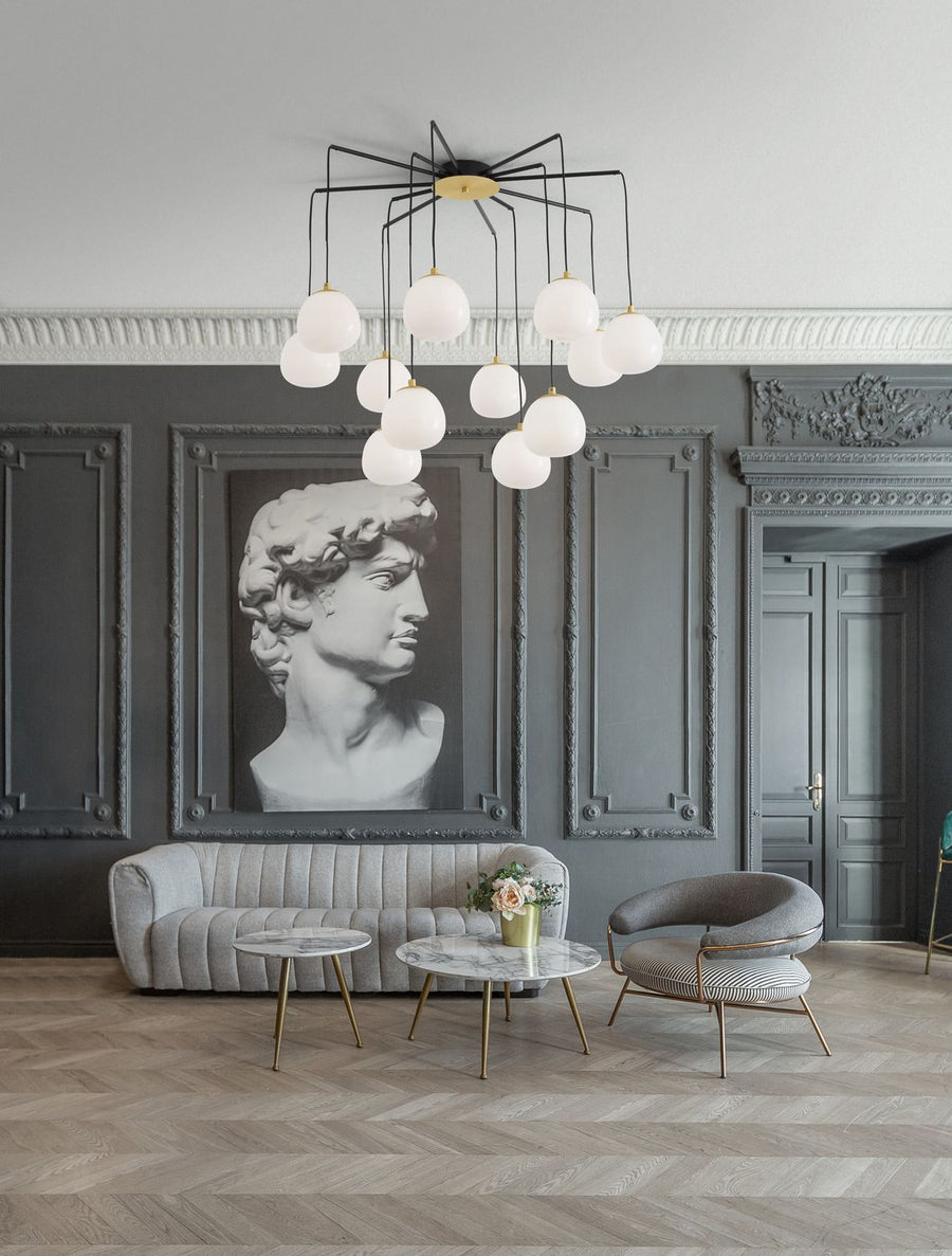 Suspension dorée installée dans un salon gris à moulures, devant un tableau sculptural