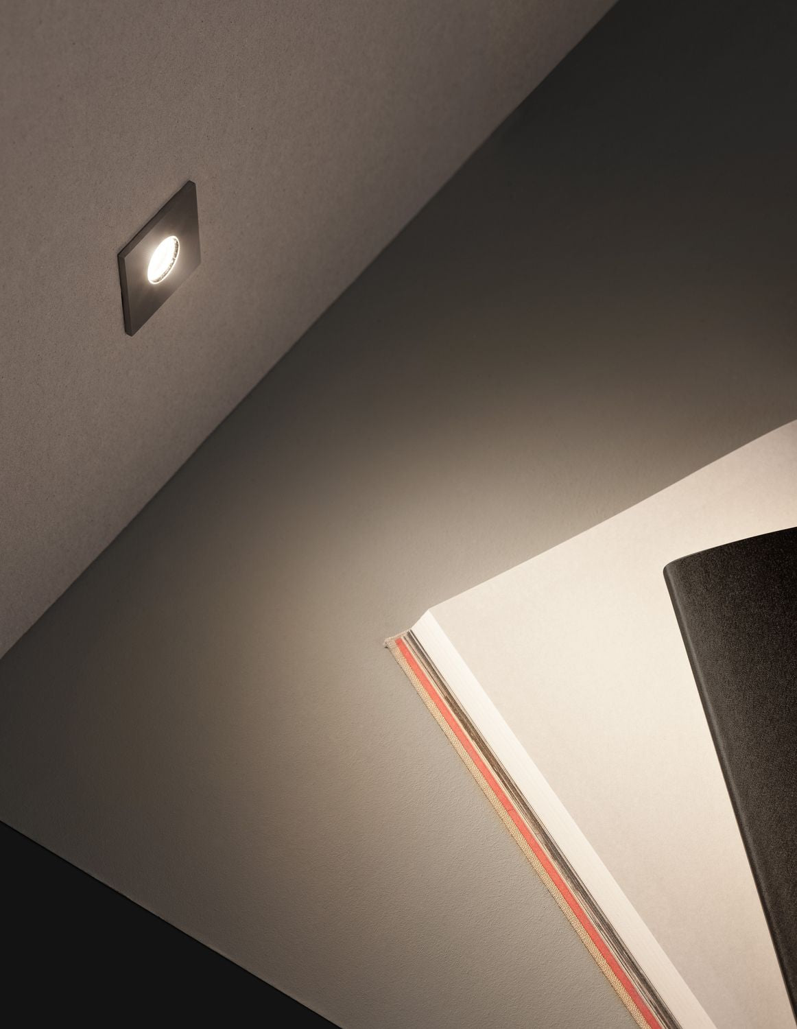Spot encastré carré installé au plafond, éclairant une pièce sombre avec un faisceau dirigé.