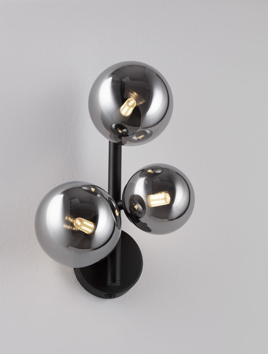 Applique murale noire avec trois globes en verre fumé allumés, vue de face