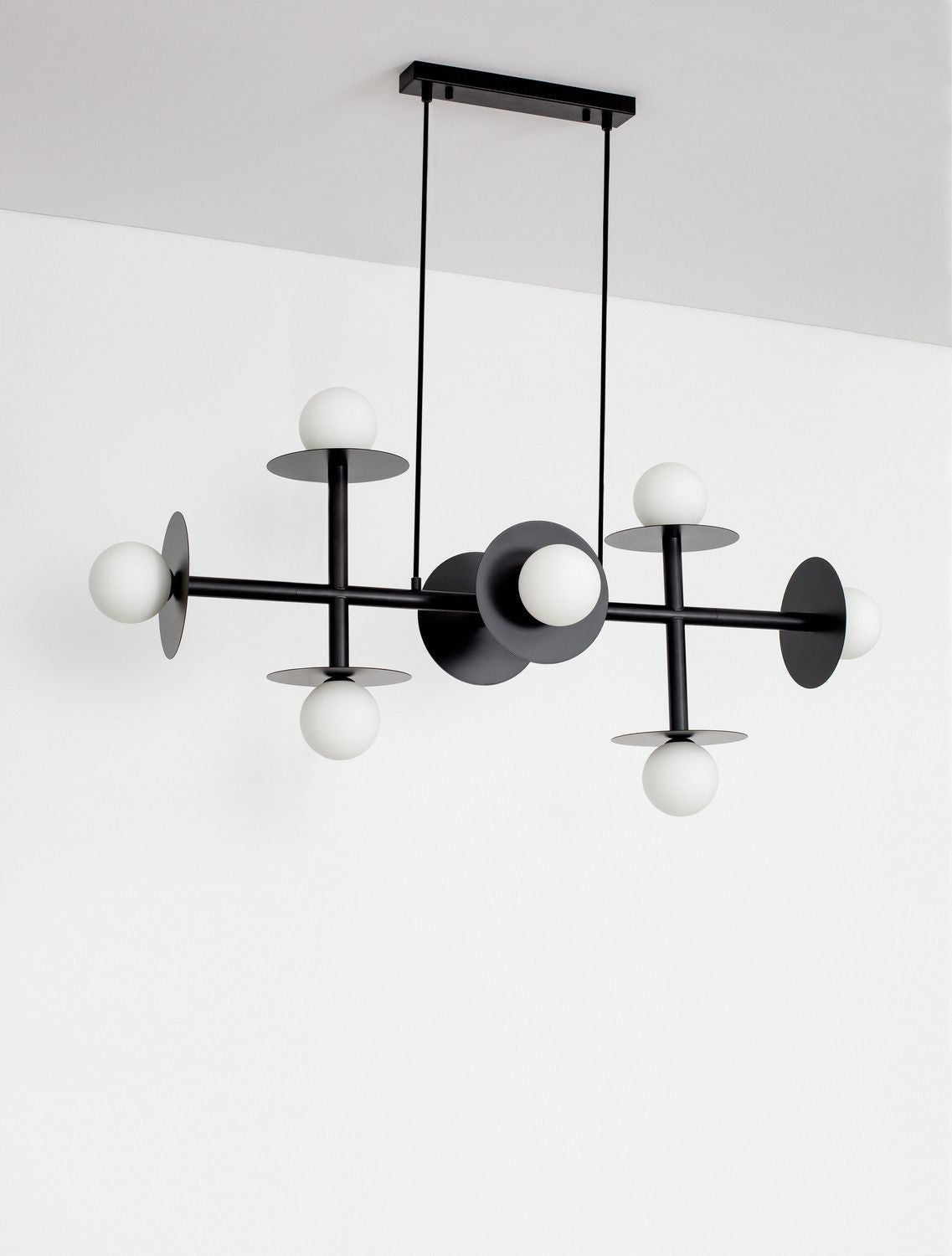 Suspension noire présentée contre un mur blanc, structure géométrique et globes en verre.