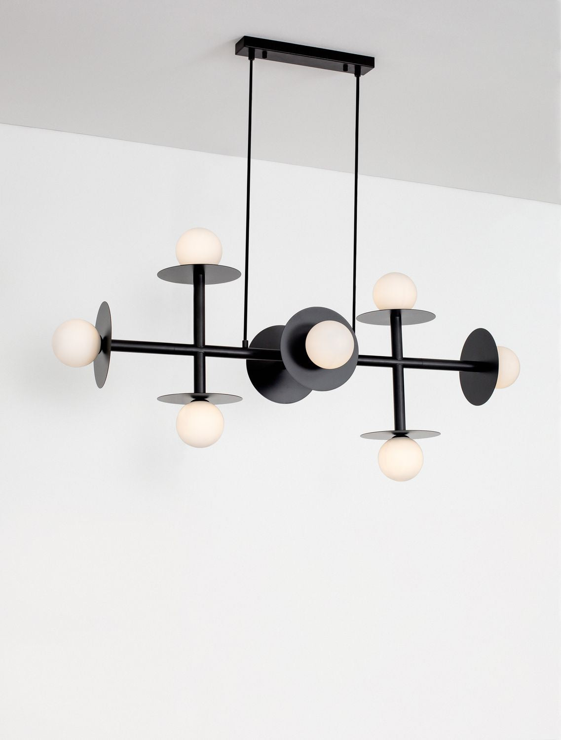 Suspension allumée contre un mur blanc, les huit globes diffusent une lumière chaude.