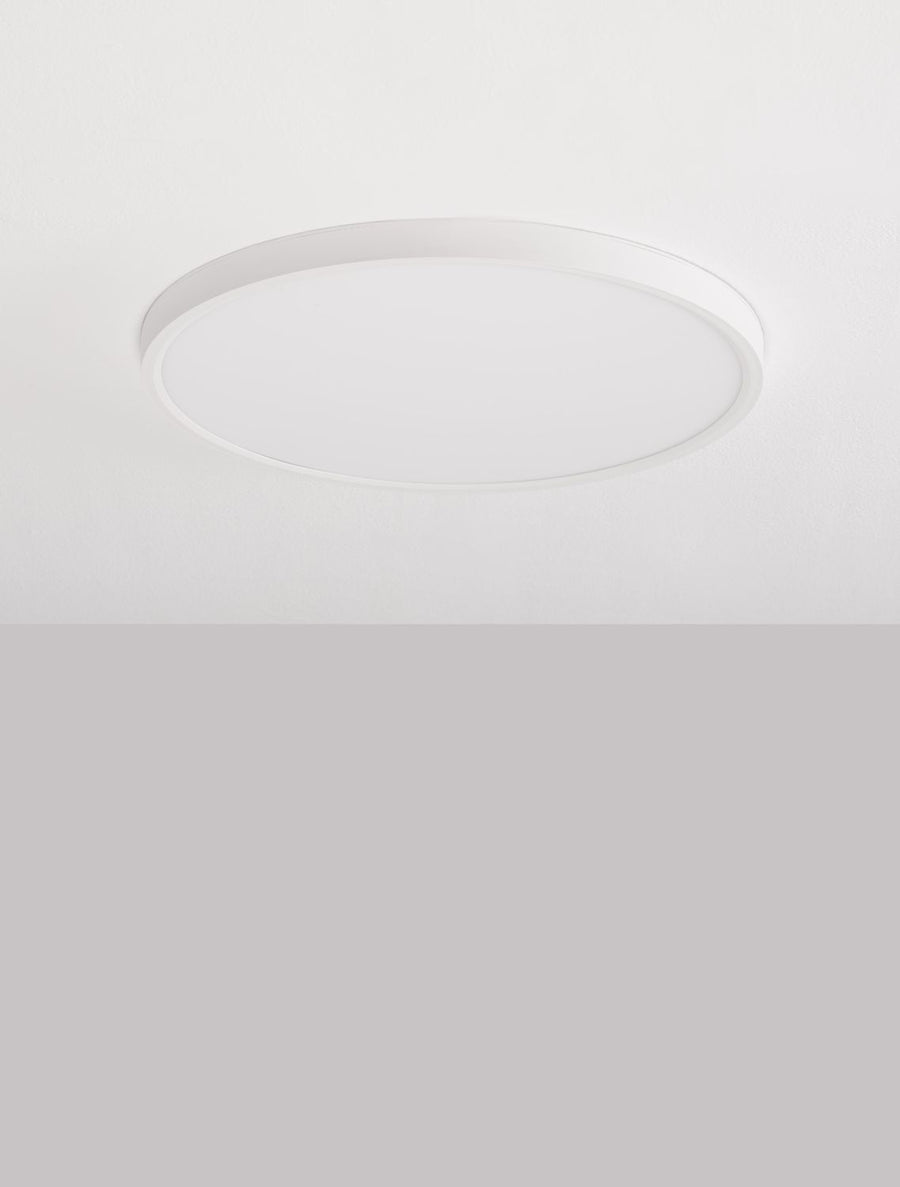 Plafonnier rond blanc éteint, posé au ras d'un plafond blanc mat