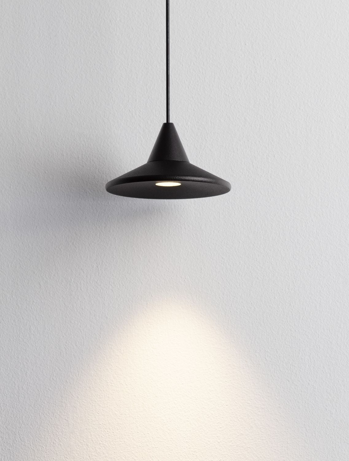 Abat-jour noir projetant un halo de lumière blanche sur le mur