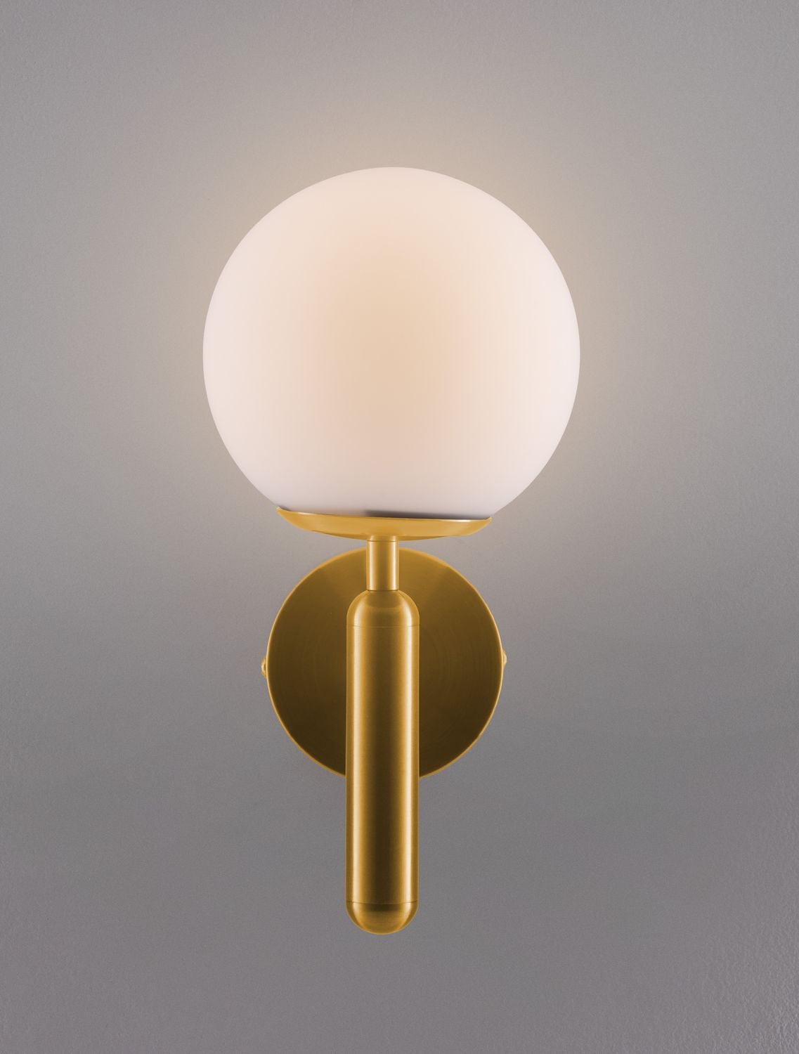 Applique dorée éclairée sur mur gris, halo lumineux doux autour du globe