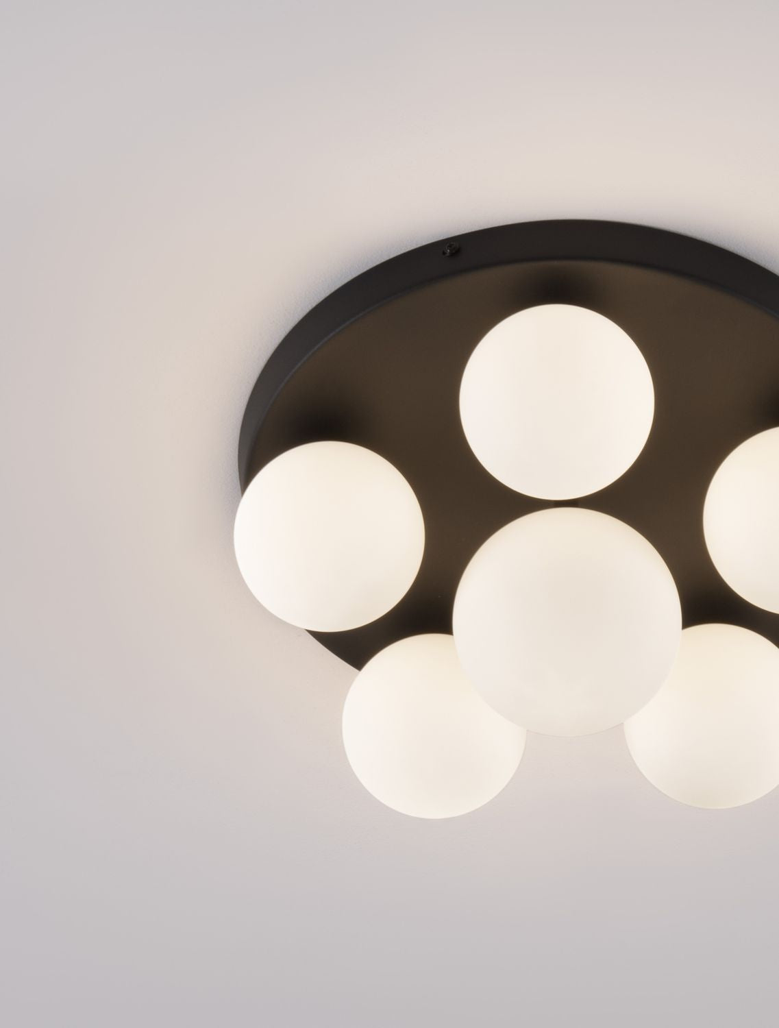 Détail rapproché de la finition noire mate et des globes en verre blanc