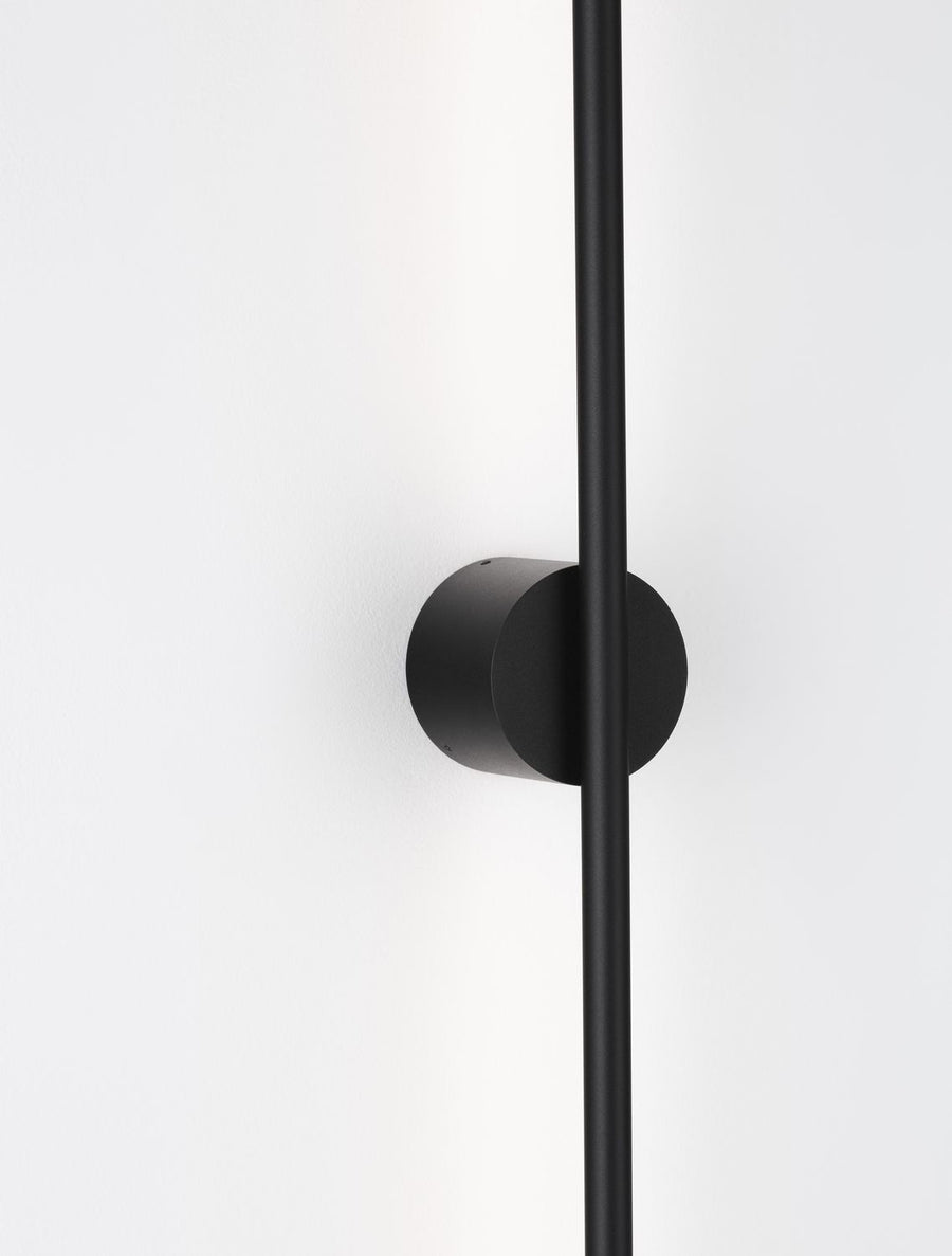Détail du socle rond noir et du tube vertical fixé au mur blanc