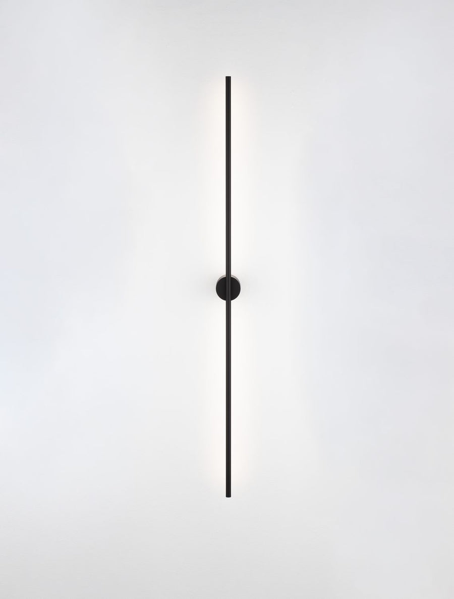 Luminaire allumé diffusant un halo lumineux vertical sur le mur blanc