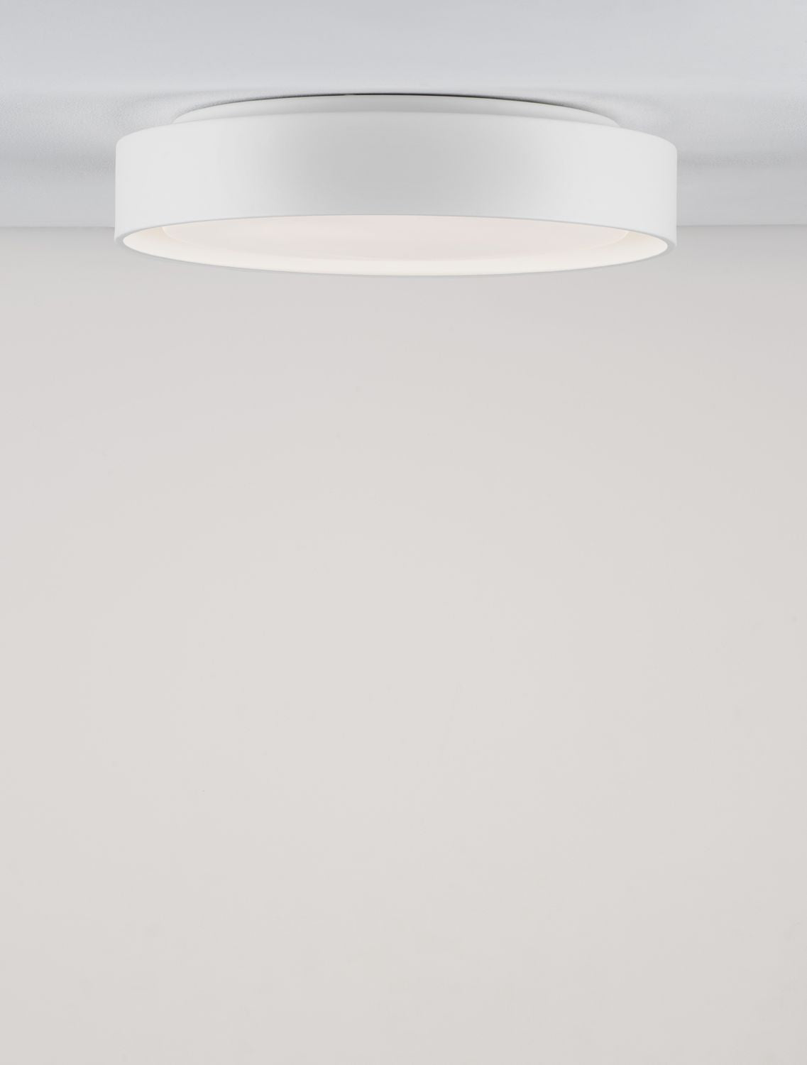 Vue en légère contre-plongée du plafonnier blanc fixé, halo lumineux périphérique visible.