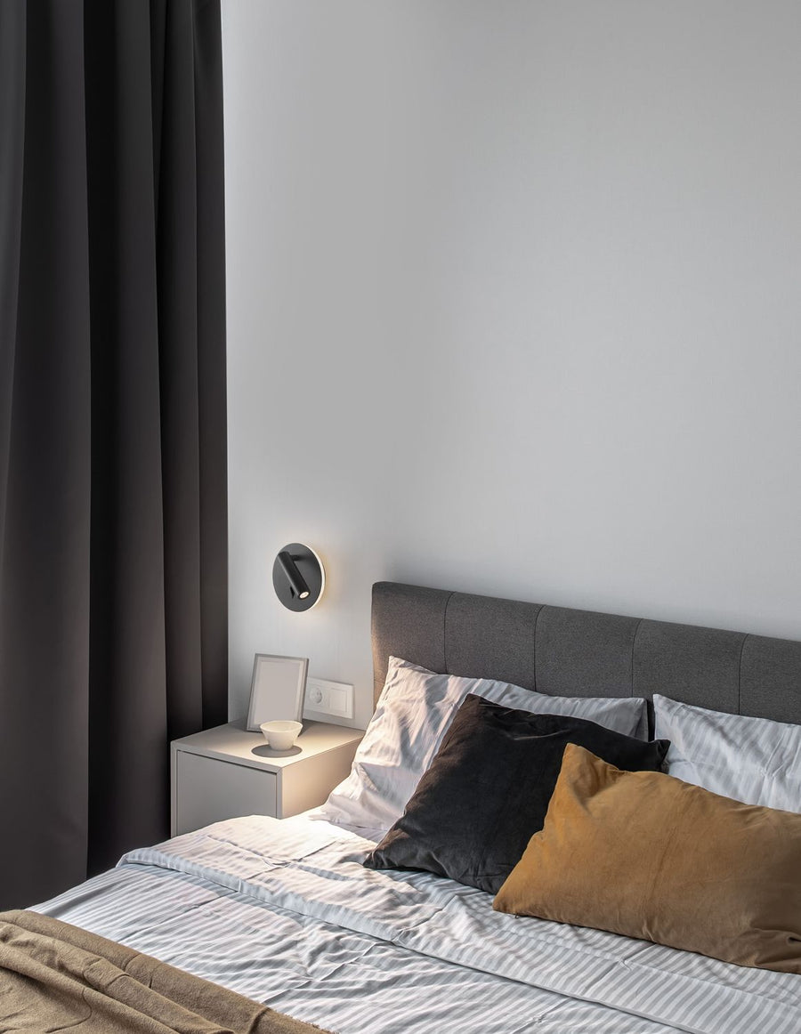 Applique murale noire allumée dans une chambre, au-dessus d'une table de chevet