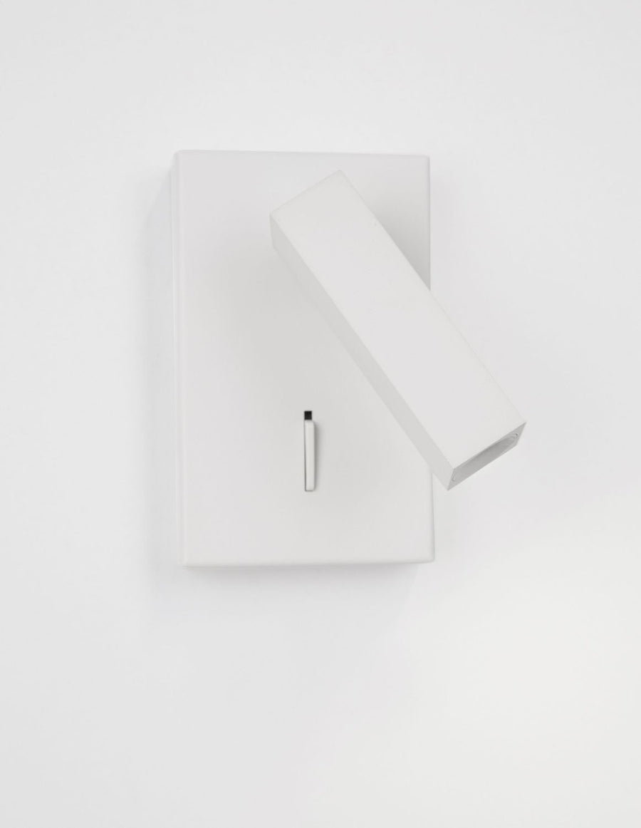 Vue de trois-quarts du luminaire blanc, boîtier rectangulaire et projecteur cylindrique orientable, interrupteur visible.