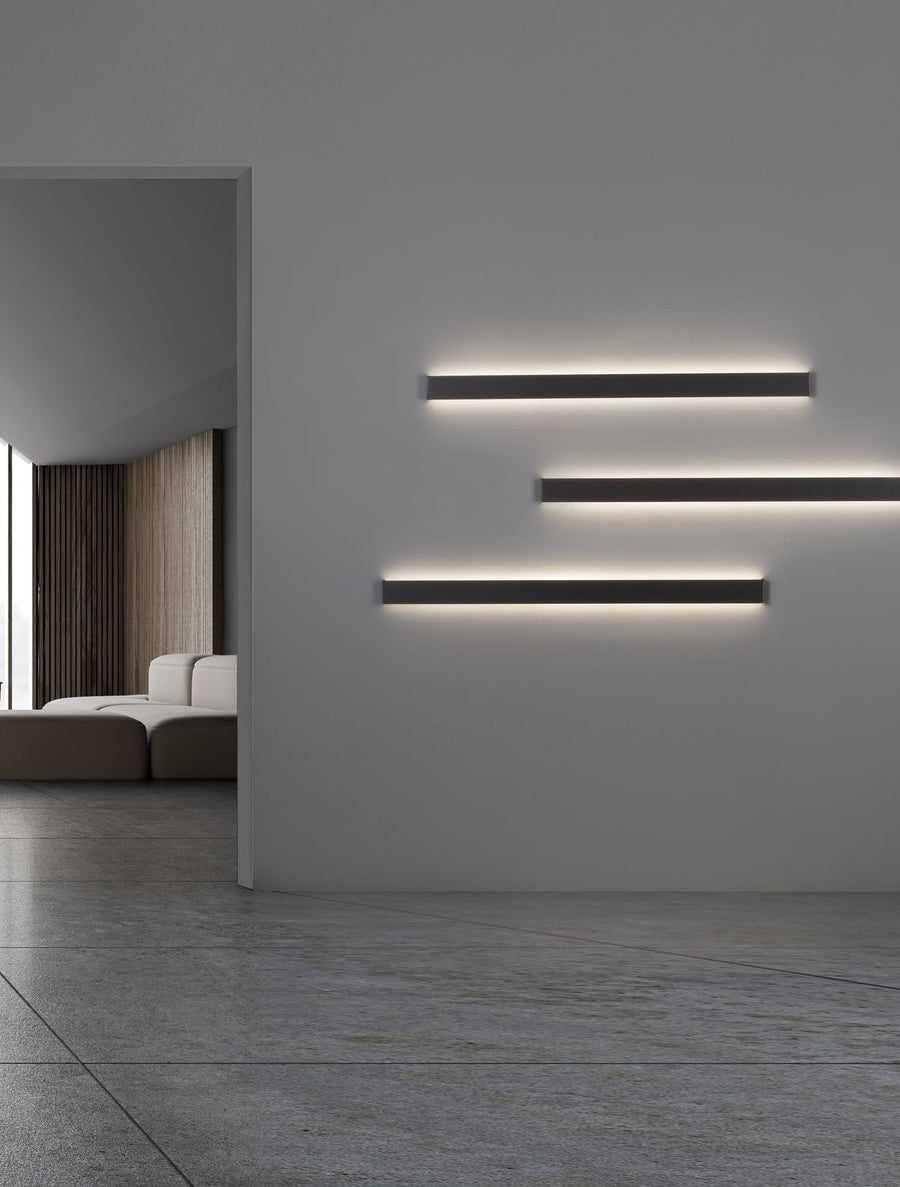 Trois appliques murales noires horizontales éclairant un mur gris dans un intérieur minimaliste