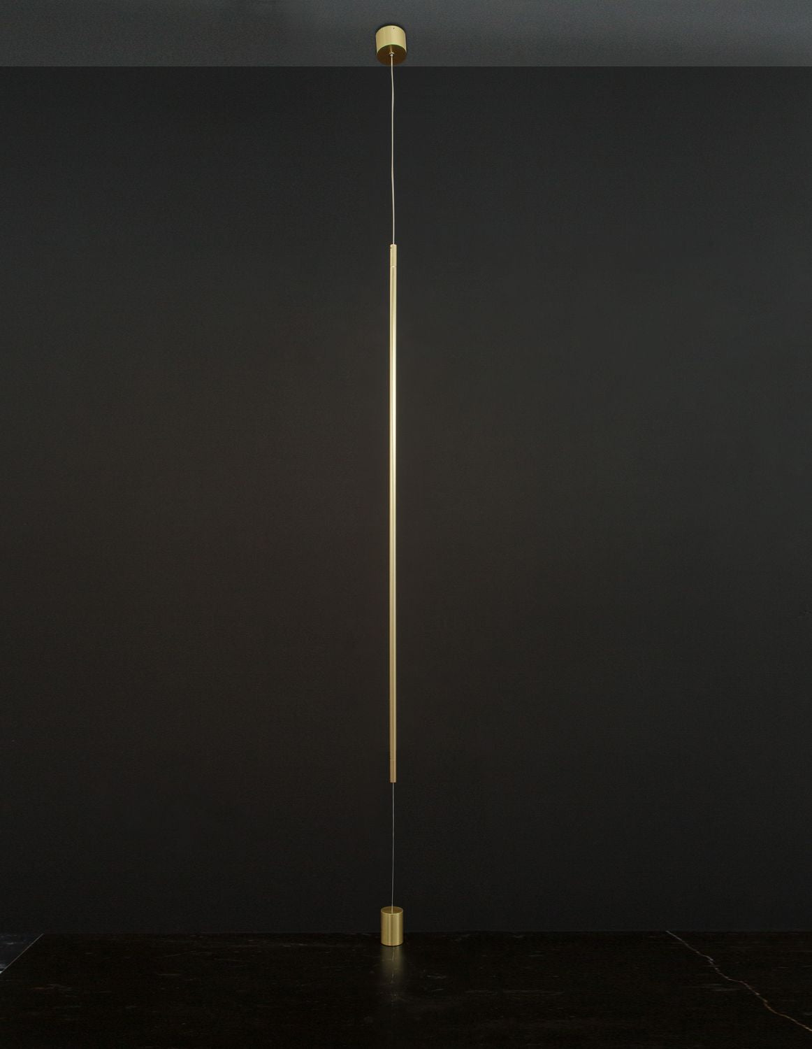 Suspension laiton installée devant un mur noir, éclairage vertical discret.