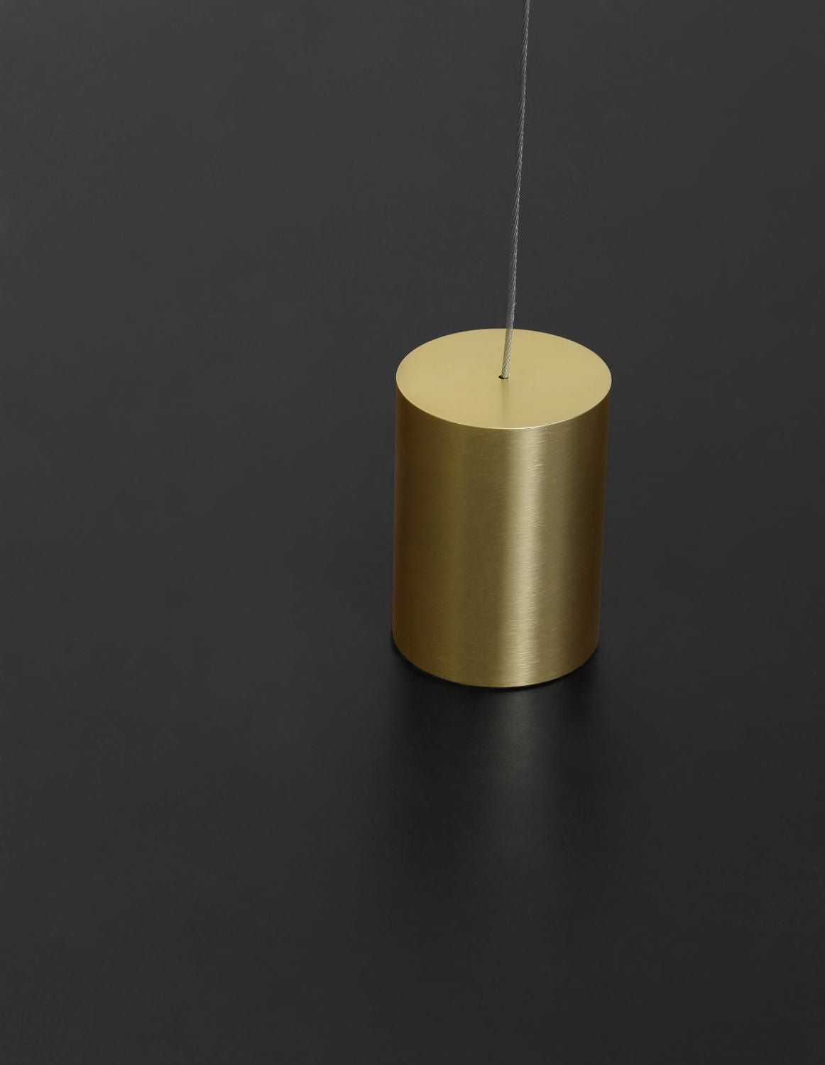 Gros plan sur le contrepoids cylindrique en laiton brossé et son câble.