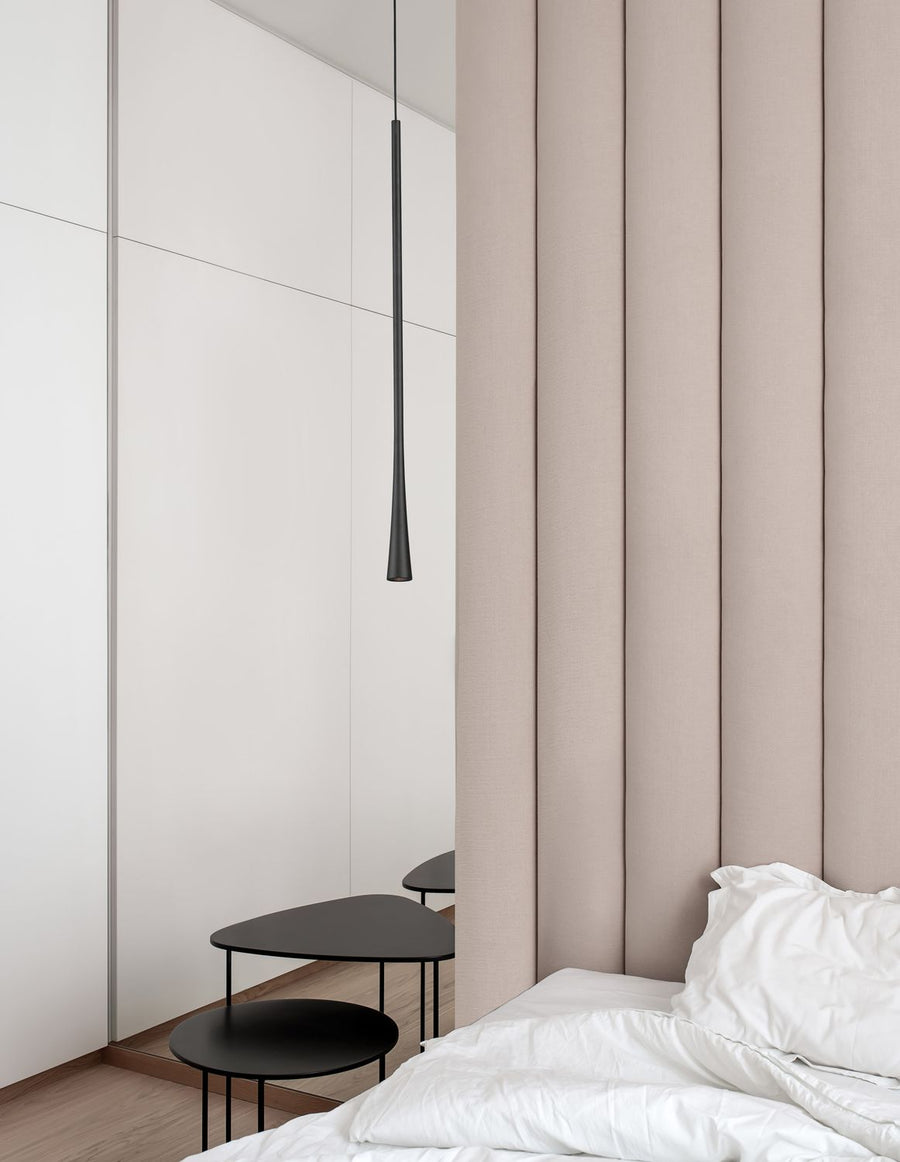 Suspension noire fine éclairant une chambre minimaliste aux murs clairs et lit blanc
