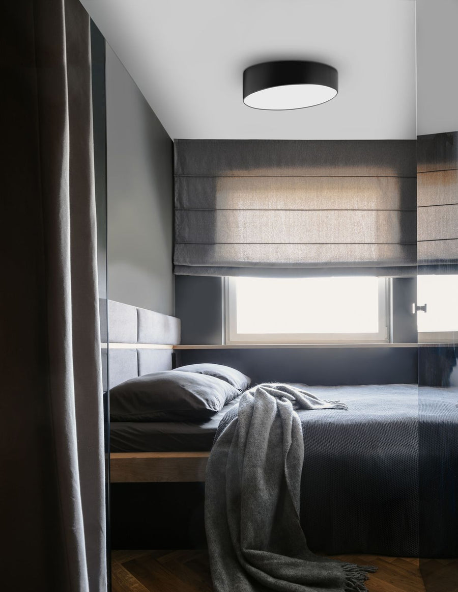 Plafonnier noir allumé au plafond d'une chambre grise, au-dessus du lit