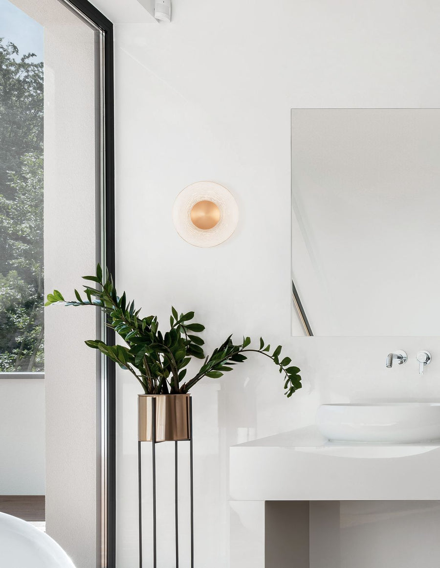 Applique murale dorée ronde fixée sur un mur blanc dans une salle de bain moderne.