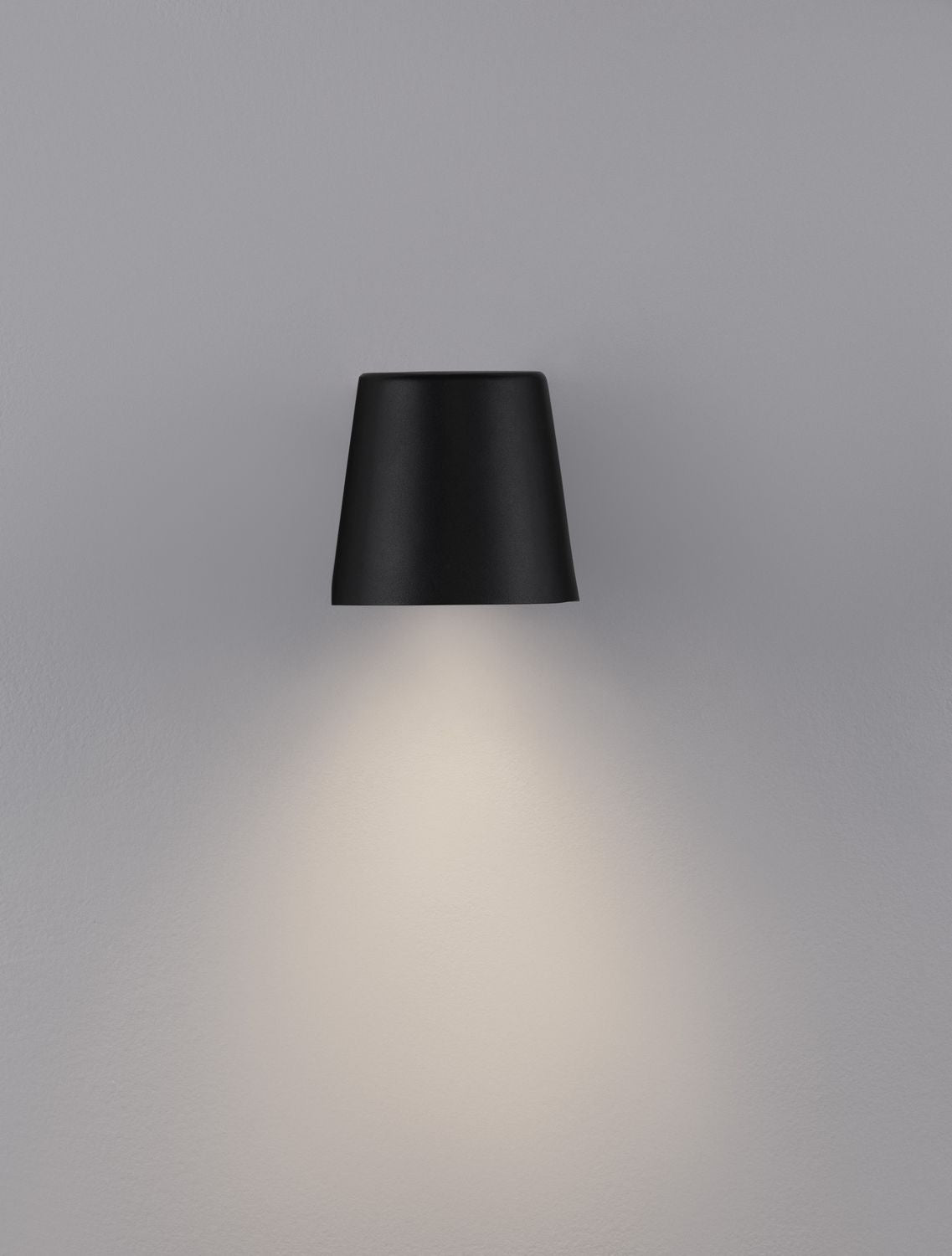 Applique allumée projetant un halo de lumière chaude vers le bas sur le mur