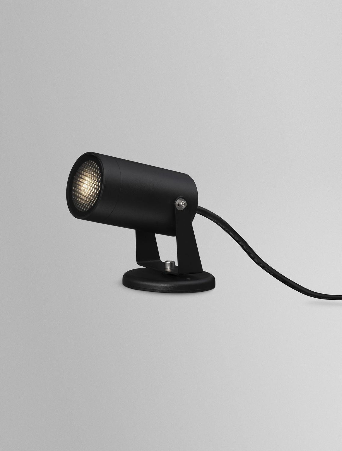 Projecteur noir allumé, lentille striée diffusant une lumière chaude en studio